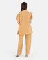 A woman viewed from the back wearing a matching tan two-piece set with a short-sleeve top featuring ruffle details on the sleeves and straight-leg pants, set against a plain light gray background.