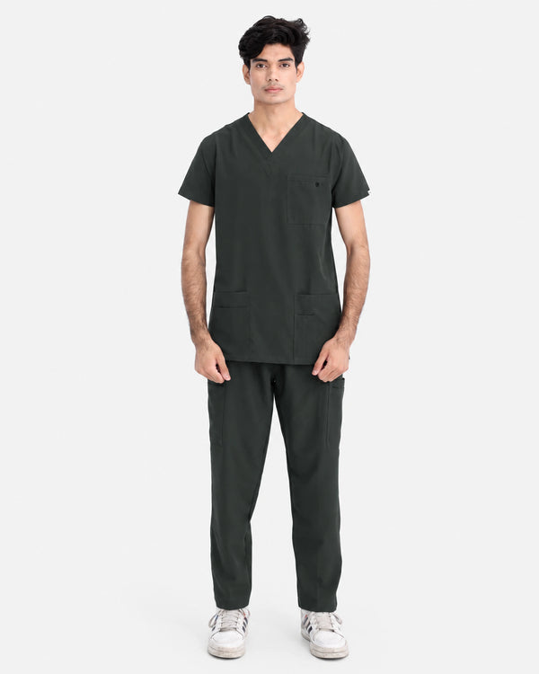 A man modeling a dark gray V-neck scrub top and matching scrub pants against a light gray studio background.