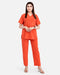 A woman modeling a bright orange scrub set consisting of a short-sleeve V-neck top and matching straight-leg pants, photographed against a plain light gray studio background.