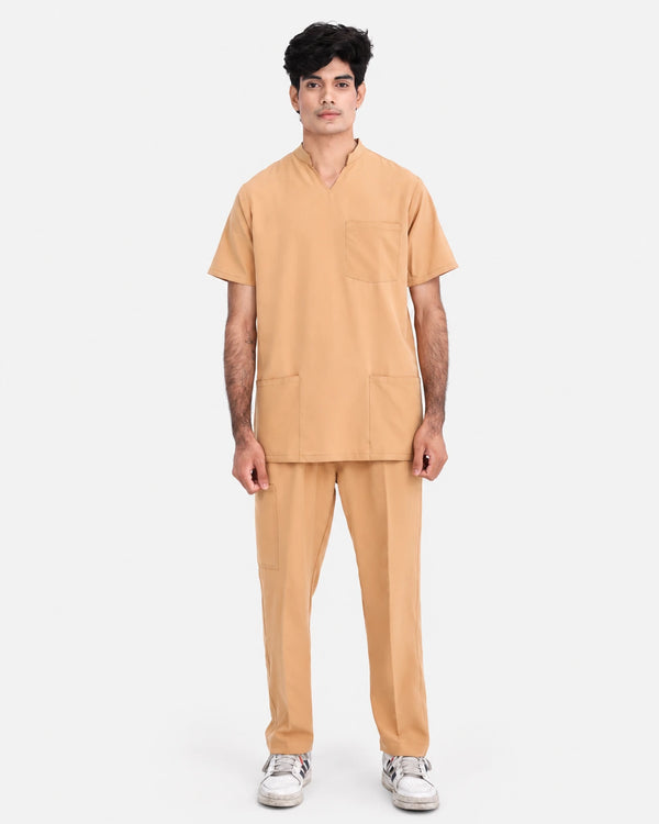 A man modeling a matching two-piece medical scrub set in a warm tan color, featuring a short-sleeve V-neck top with a chest pocket and matching straight-leg pants, set against a plain light gray background.