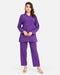 A woman modeling a matching purple two-piece scrub set consisting of a long-sleeve V-neck top and straight-leg pants, photographed against a light gray studio background.