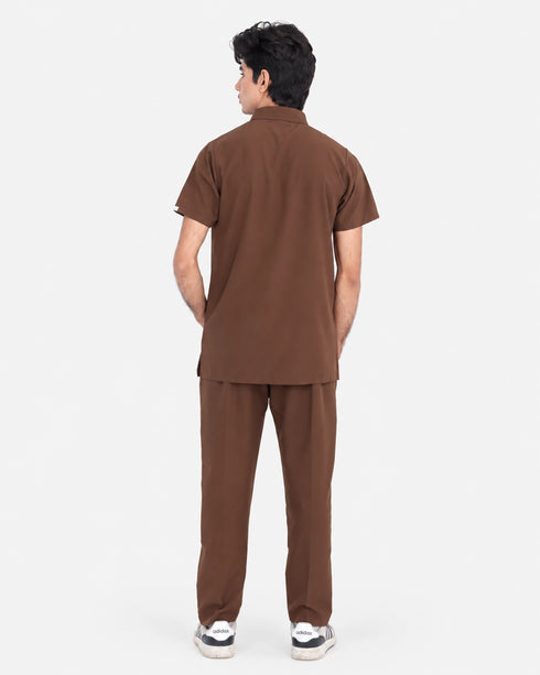 A man viewed from the back wearing a matching brown short-sleeve shirt and trousers set, standing against a plain light gray studio background.