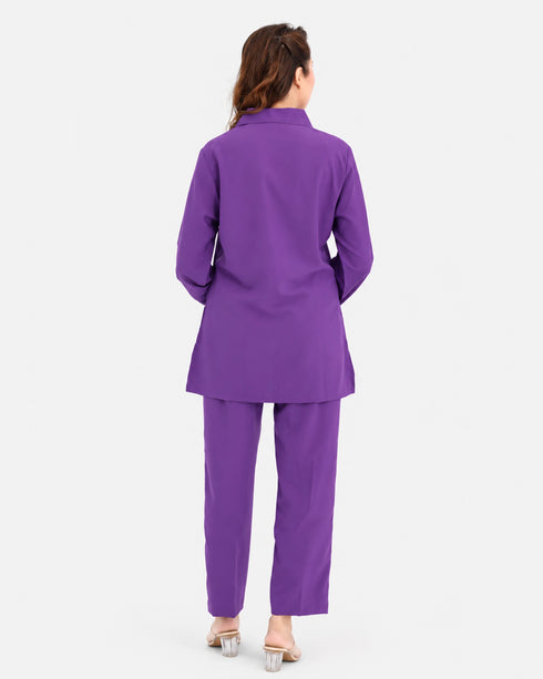 A woman viewed from the back wearing a matching purple blazer and trouser set, standing against a plain light gray studio background.
